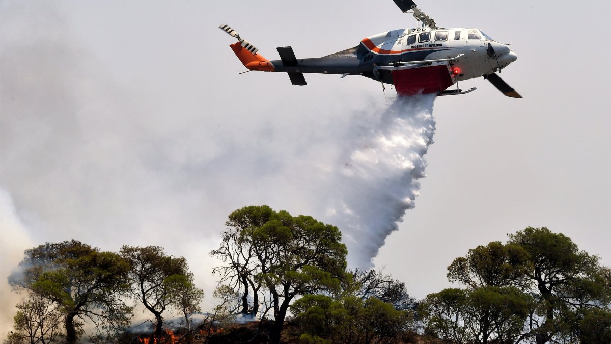 Un avión de extinción de incendios arroja agua para extinguir un incendio forestal que está quemando una zona forestal frente a las instalaciones de la refinería de Motor Oil, Grecia.