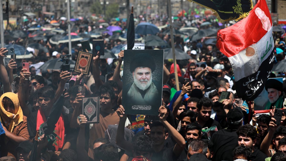 Los musulmanes chiítas iraquíes cantan eslóganes y llevan una imagen de Muqtada al-Sadr y copias del Corán mientras el humo está en el aire durante una reunión en Bagdad, Irak.