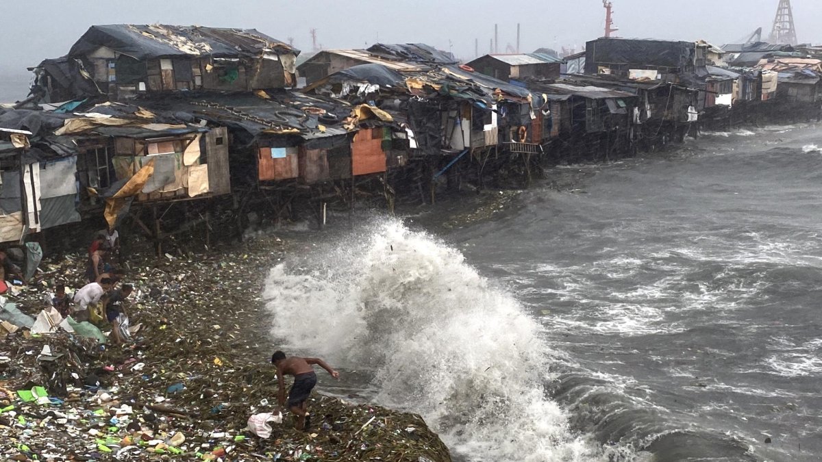 Un hombre se ve sorprendido por una ola mientras rescata materiales desperdigados por la orilla en Manila Bay, Filipinas, este miércoles.
