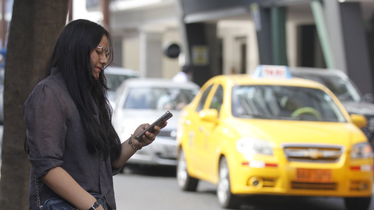 Usuaria. Una joven solicita un taxi mediante una aplicación y analiza al chofer antes de aceptar ese carro.