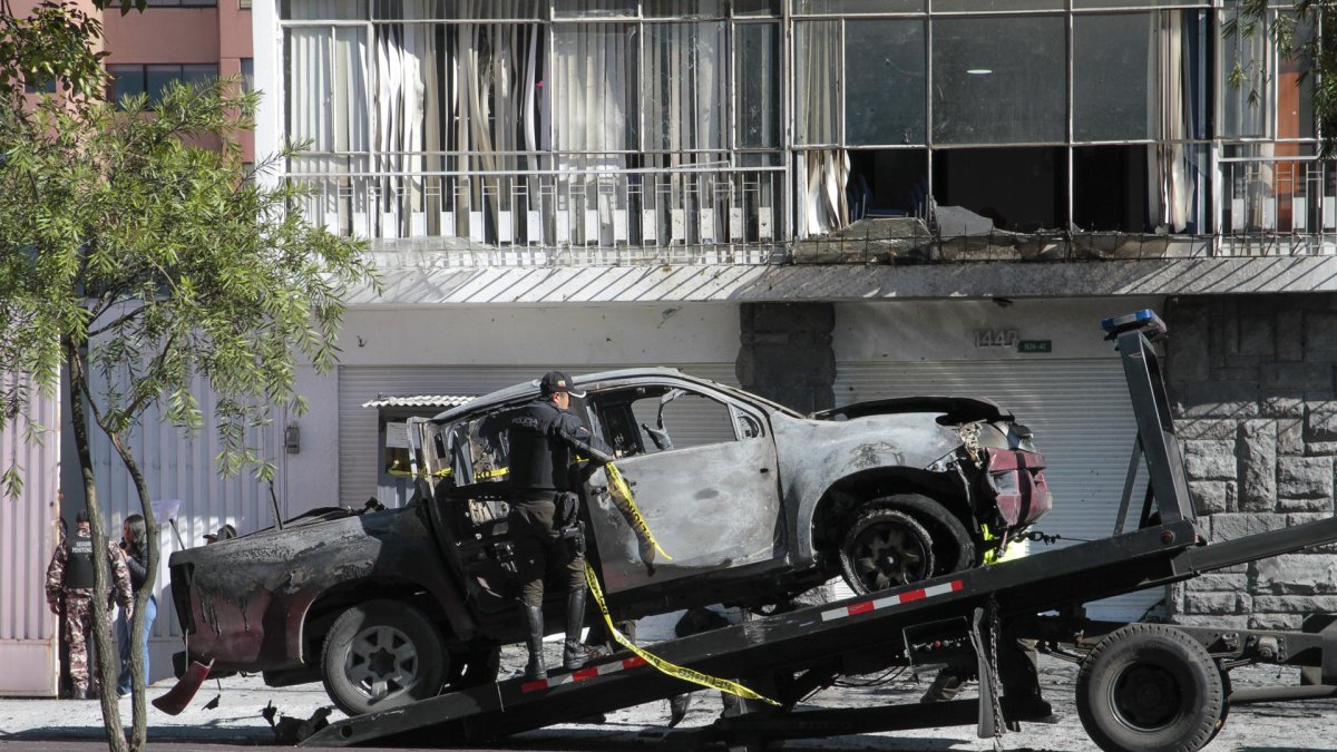 Un policía carga en una grúa los restos de un carro bomba que explotó en los exteriores del edificio del Servicio Nacional de Atención Integral a Personas Privadas de Libertad (SNAI), en Quito (Ecuador).