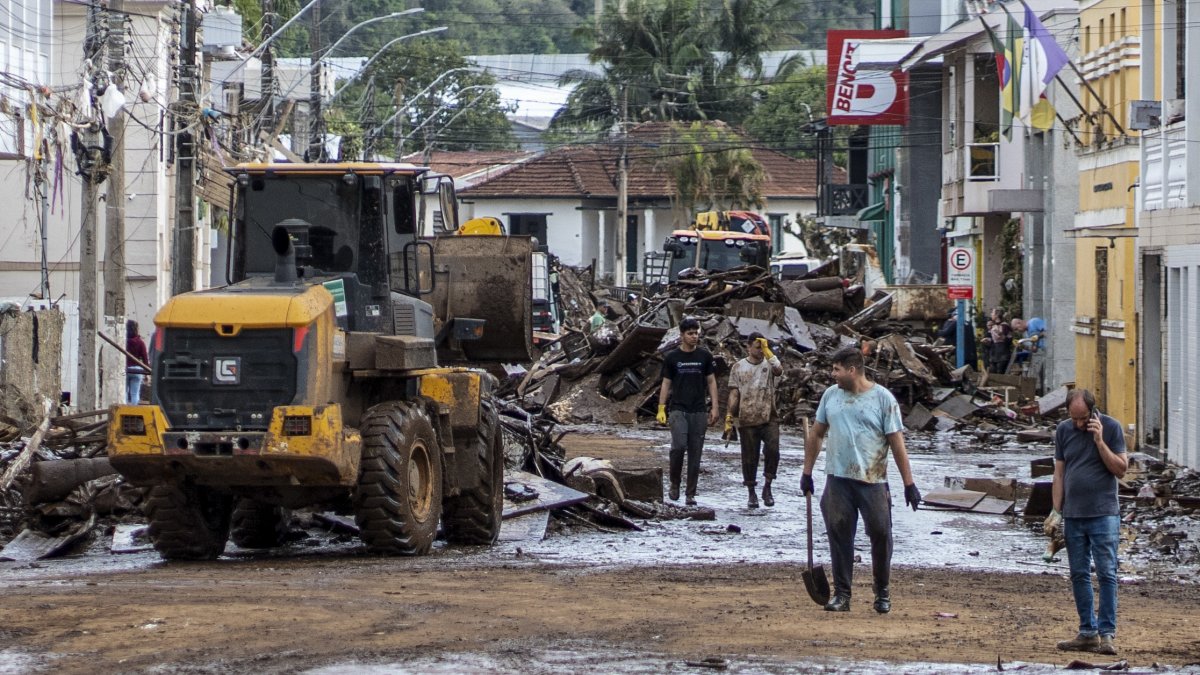 Personas junto a un vehículo de maquinaria pesada mientras despejan una calle inundada por las torrenciales lluvias, en Muçum, estado de Rio Grande do Sul (Brasil).