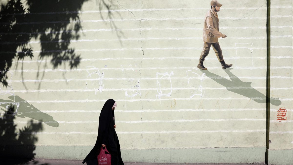 Imagen de archivo de una mujer con velo que pasa junto a una pared con un soldado iraní pintado en ella en una calle de Teherán.