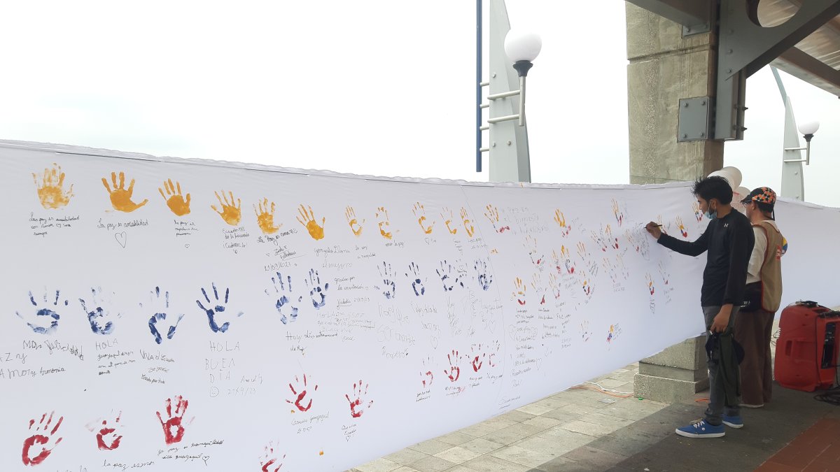 Personas acuden para dejar su huella de la mano en colores de la bandera sobre la tela y escribir un mensaje de paz