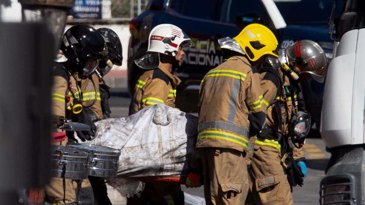 Bomberos trasladan el cuerpo de un fallecido en el incendio este domingo.