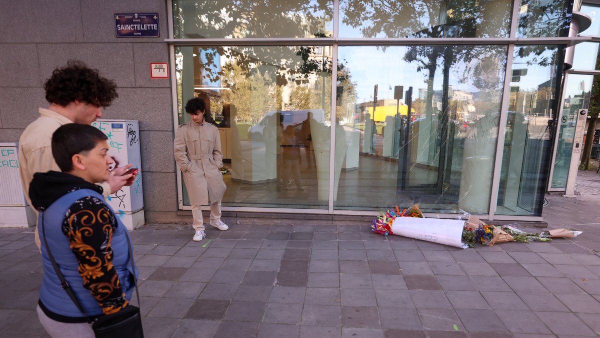 Un grupo de personas observa el ramo de flores colocados en el sitio donde dos personas fueron atacadas este lunes 16 de octubre de 2023 en Bruselas.