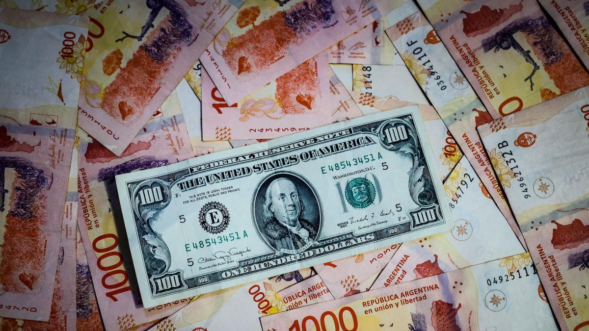 Fotografía de archivo de comparativa de billetes de pesos argentinos con un billete de 100 dolares estadounidenses.