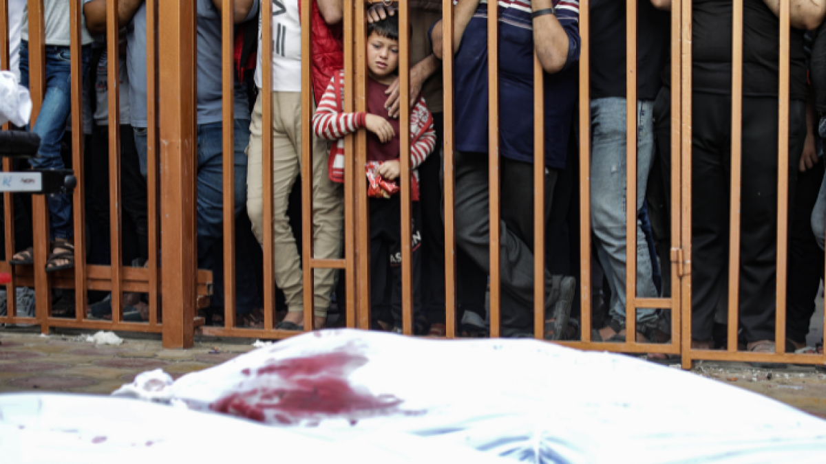 Un niño palestino observa tras unos barrotes los cadáveres de las víctimas cubiertos con sábanas en el hospital Nasser en Khan Yunis, al sur de la Franja de Gaza