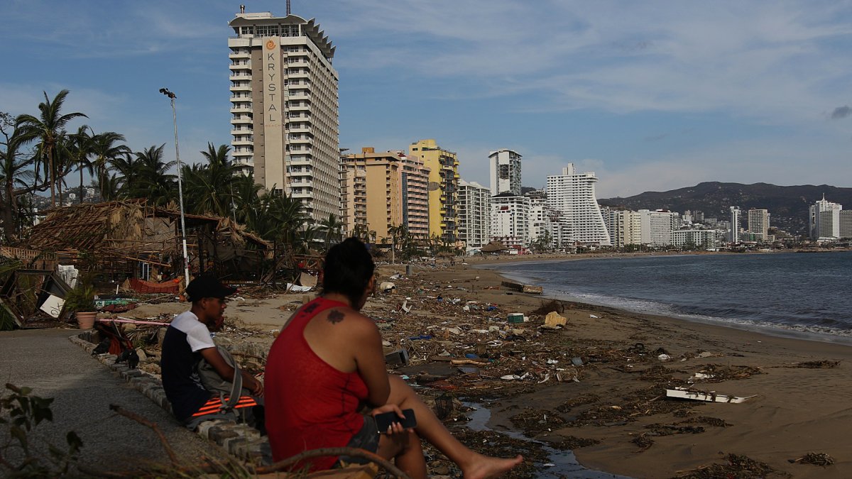 Personas permanecen sentadas junto a los escombros causados por el huracán Otis hoy, en el balneario de Acapulco, en el estado de Guerrero (México)