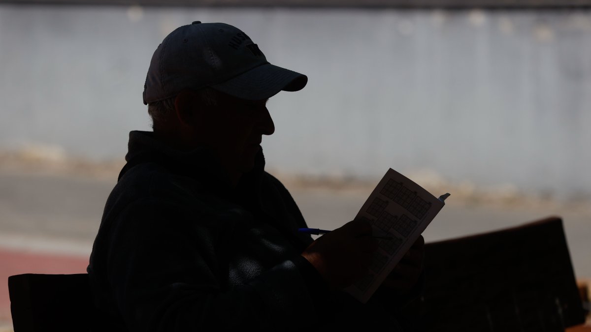 Fotografía de archivo de un hombre que lee un libro en un banco de un parque madrileño.