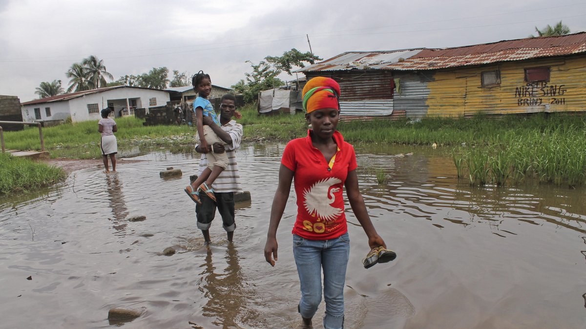 Un grupo de vecinos, con los pantalones remangados y el calzado en la mano, cruzan una zona encharcada.