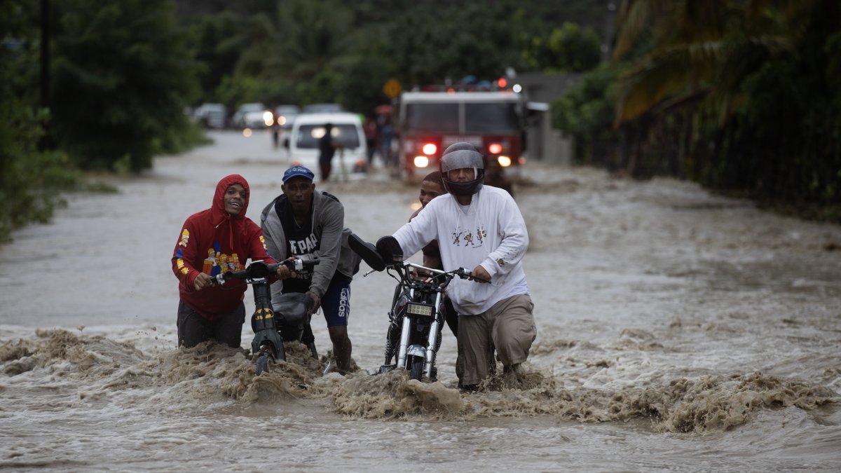 Personas cruzan con dificultad la carretera que se encuentra inundada producto de las intensas lluvias, en San José de Ocoa (República Dominicana). 