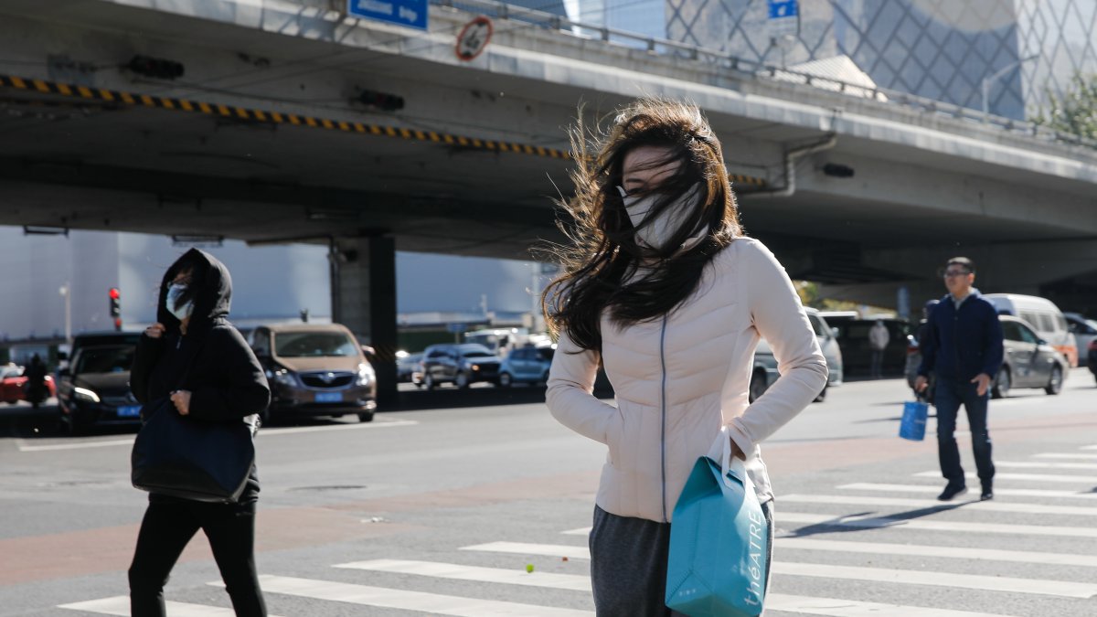 Pekín. Varias personas transitan una calle de esta capital en medio de una ola de frío y fuertes vientos.