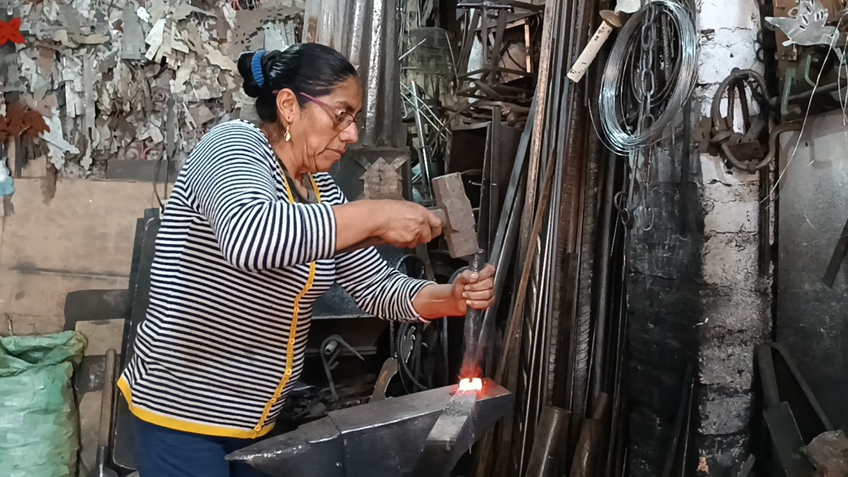 Lucila con el combo y cincel golpea una manija contra el yunque.