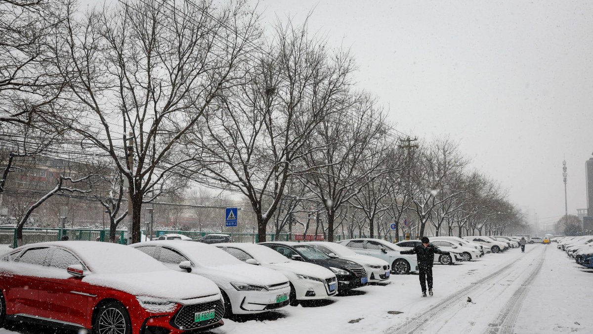 Un hombre transita por una calle en donde los carros aparecen estacionados y cubiertos bajo un manto blanco y congelado, en Pekín, este miércoles 13 de diciembre de 2023.