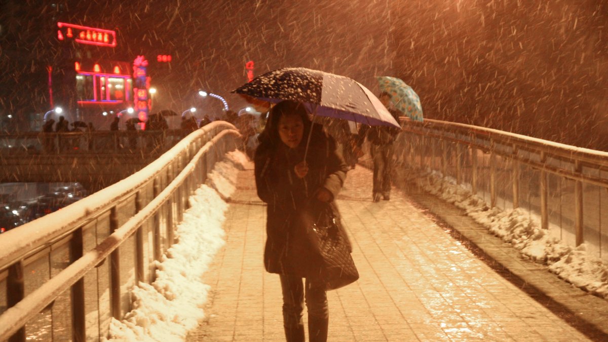 Una mujer al caminar con dificultad sobre un puente peatonal elevado y bajo una fuerte torementa de nieve en Shanghái (China).