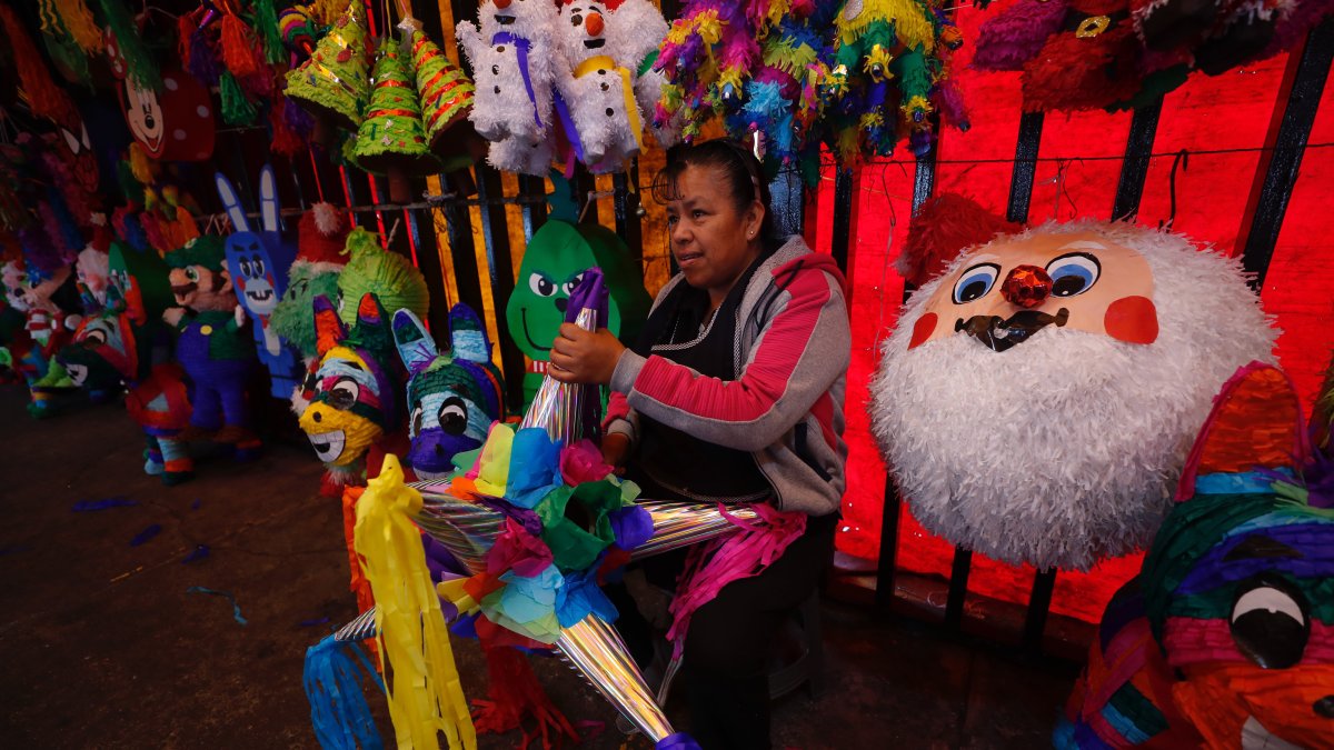 Tradición. Una vendedora sostiene una piñata en el mercado de Jamaica, en Ciudad de México y habla sobre las ventas de los productos.