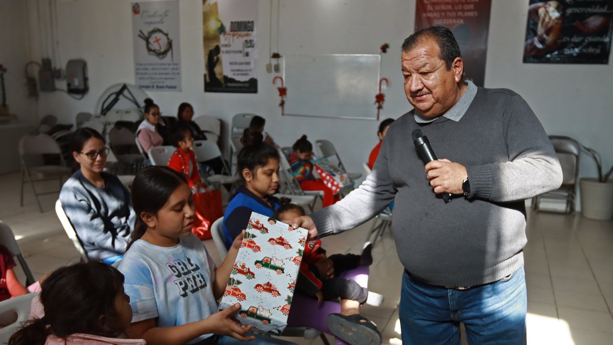 El pastor Juan Fierro (d) reparte regalos a migrantes que pasan la Navidad en el albergue 'El buen samaritano', el 24 de diciembre de 2023, en Ciudad Juárez Chihuahua (México).