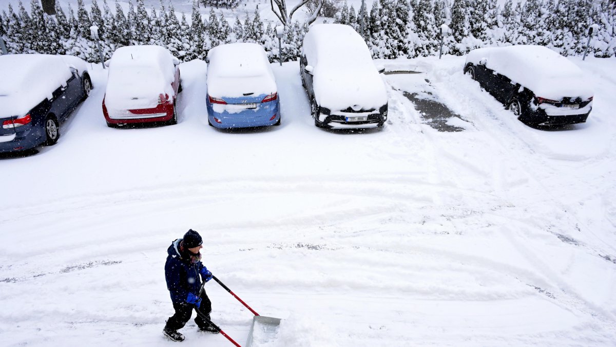 Después de una fuerte nevada, un hombre trabaja con una pala de nieve para quitar la nieve de las plazas de aparcamiento de un edificio residencial en Estocolmo (Suecia), este 5 de enero de 2024.