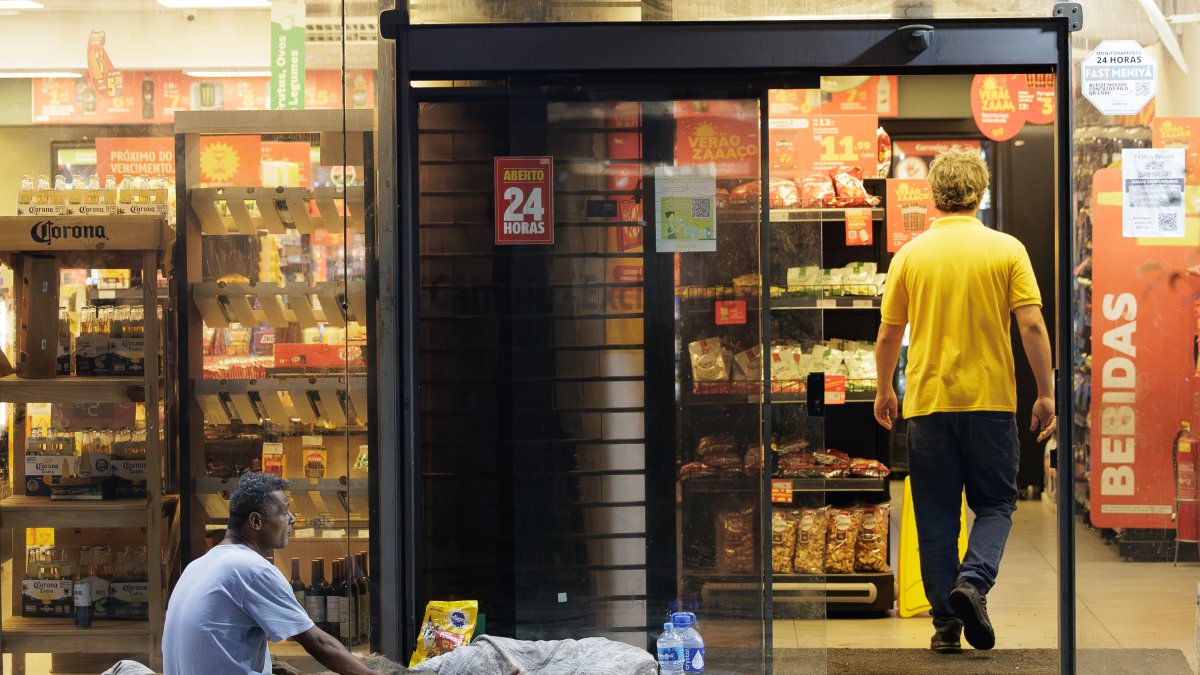 Desigualdades. Una persona en condición de calle espera ayuda de transeúntes afuera de un minimercado.