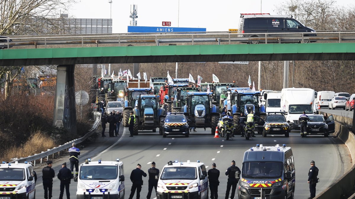 Agentes de policía vigilan decenas de tractores que participan en una manifestación en la autopista A15 cerca de Argenteuil, al norte de París, Francia, este lunes 29 de enero de 2024.