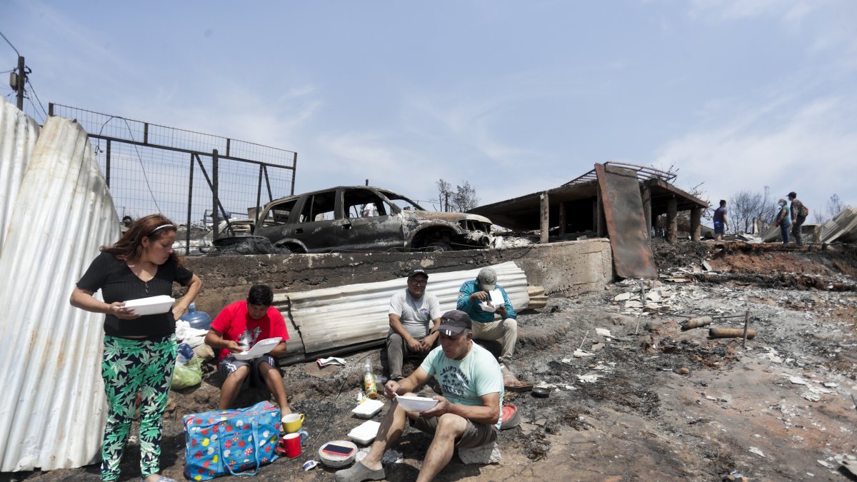 Personas del campamento irregular “Pompeya” almuerzan entre los escombros, tras los incendios del día viernes 2 de febrero, en la zona de Viña del Mar.
