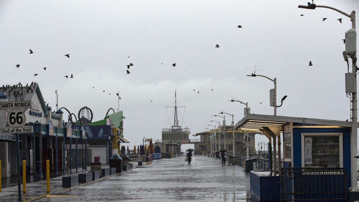Una persona recorre el muelle de Santa Mónica sosteniendo un paraguas en medio la tormenta azota el sur de California.