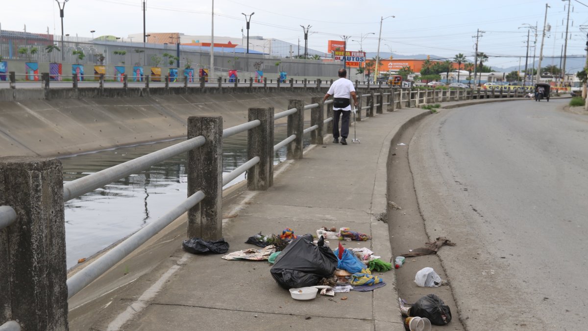 Varios ciudadanos colocan fundas con desechos junto a un canal entre las ciudadelas Las Orquídeas y Los Vergeles.