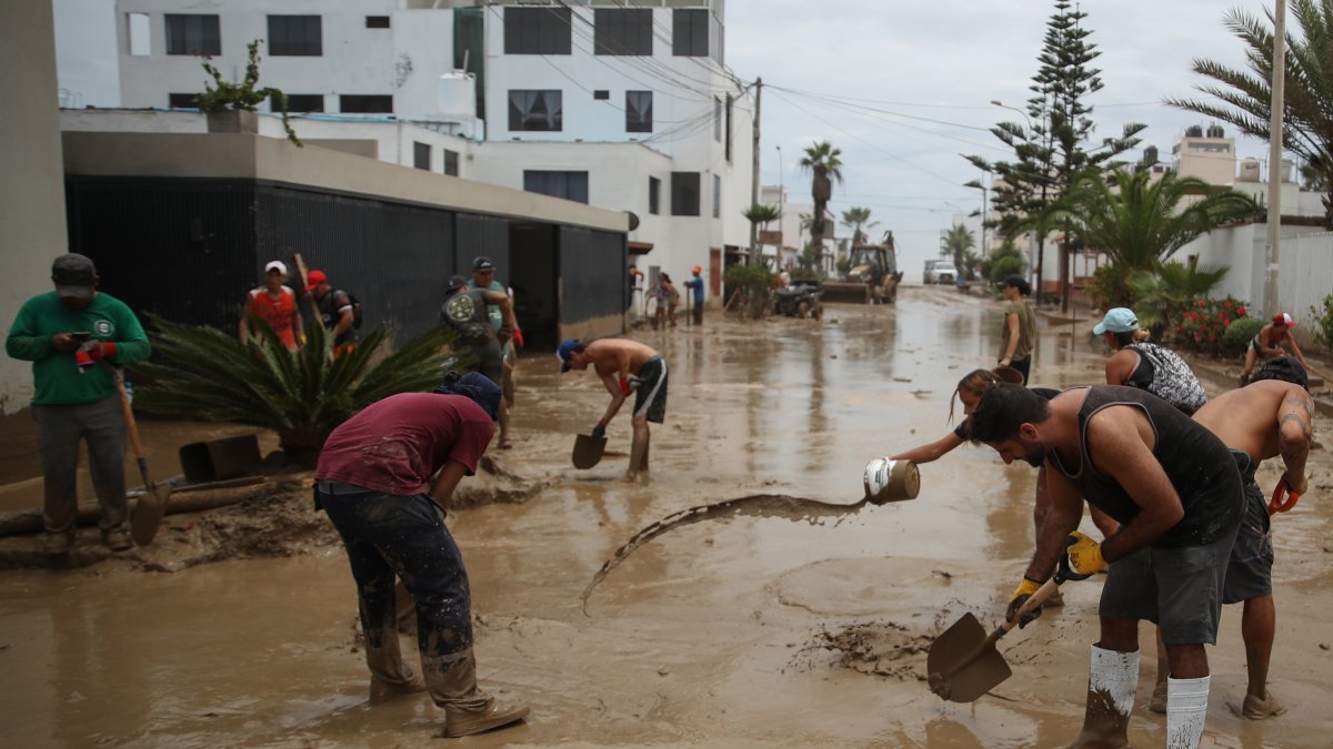 Personas ayudan a remover el lodo en una calle afectada por las lluvias, en Lima (Perú), en una fotografía de archivo.