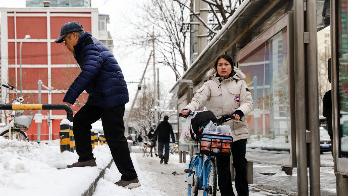 La gente espera un autobús en la calle después de una Nevada en Beijing, China, 21 de febrero de 2024.