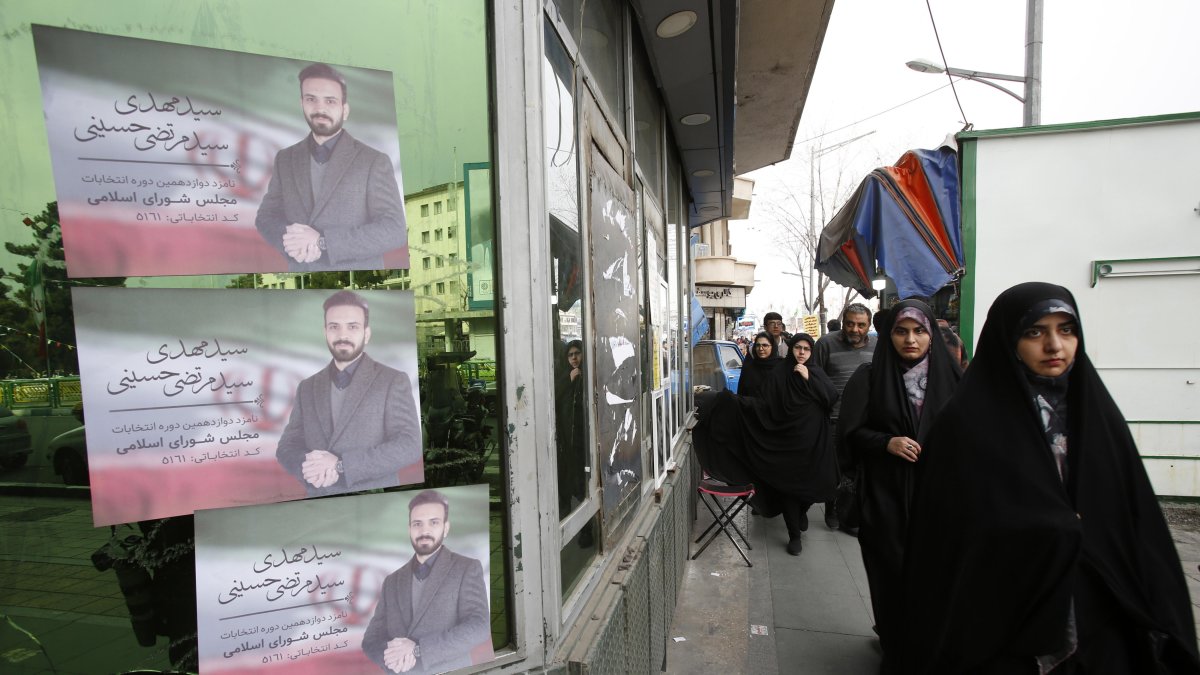 Mujeres iraníes con velo caminan junto a carteles de campaña electoral de candidatos parlamentarios durante el primer día de las campañas electorales