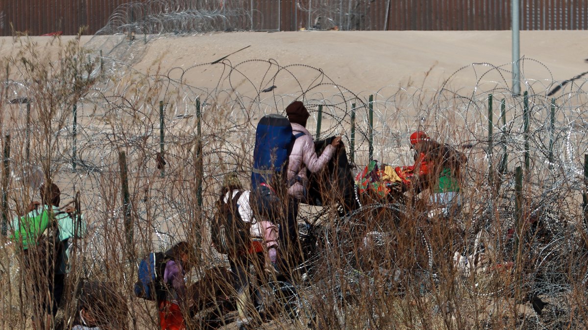 Migrantes intentan cruzar la cerca de alambres en la frontera que divide a México de los Estados Unidos.