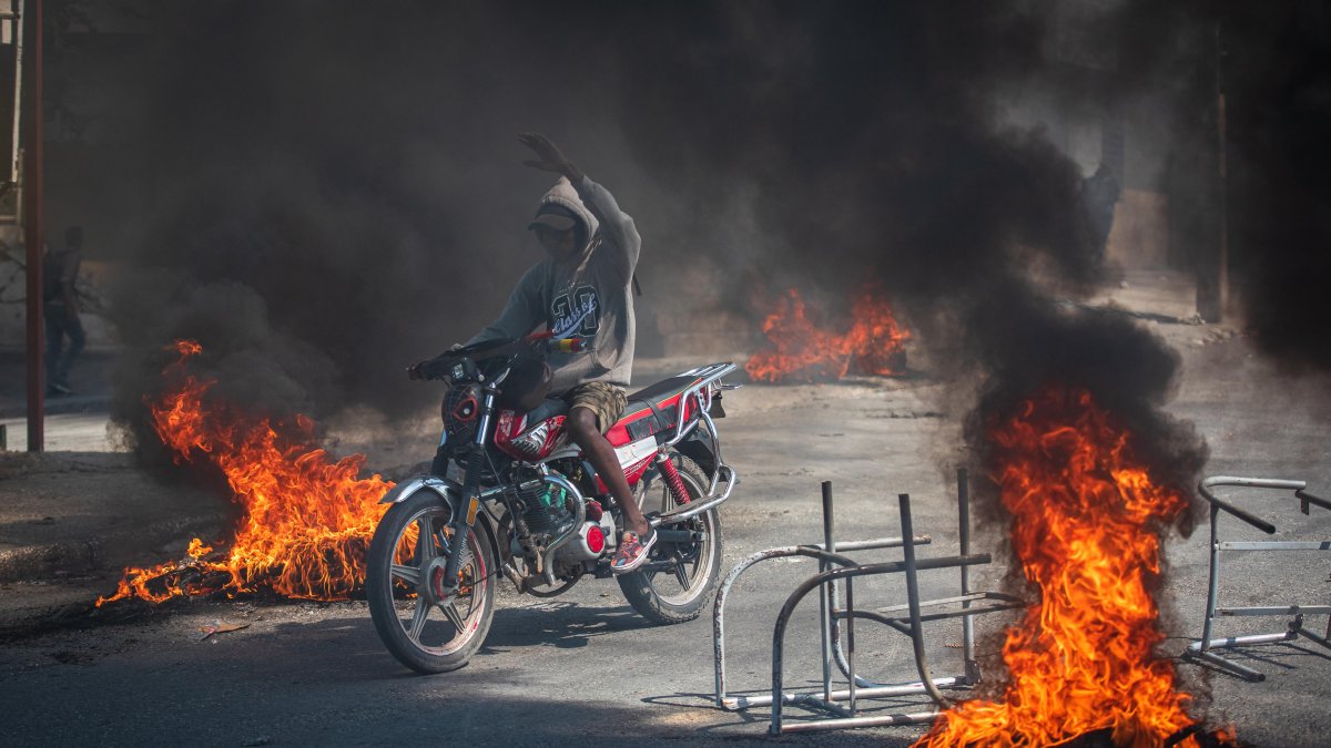 Una persona se transporta en motocicleta con incendios alrededor, este viernes en Puerto Príncipe (Haití).