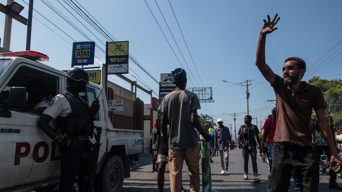 Manifestantes contra la situación política y social de Haití tras la renuncia del primer ministro Ariel Henry pasan junto a un carro policial.