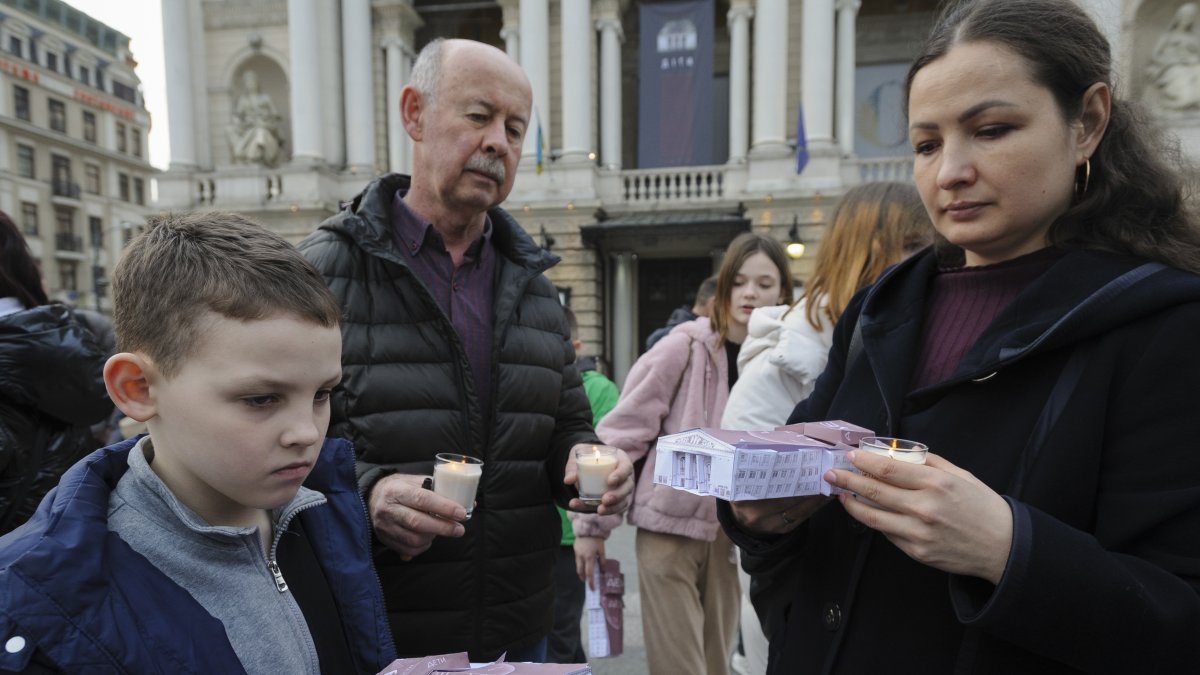 La gente sostiene velas y pequeños modelos del teatro durante una manifestación conmemorativa para conmemorar el segundo aniversario del bombardeo del Teatro Dramático Mariupol.