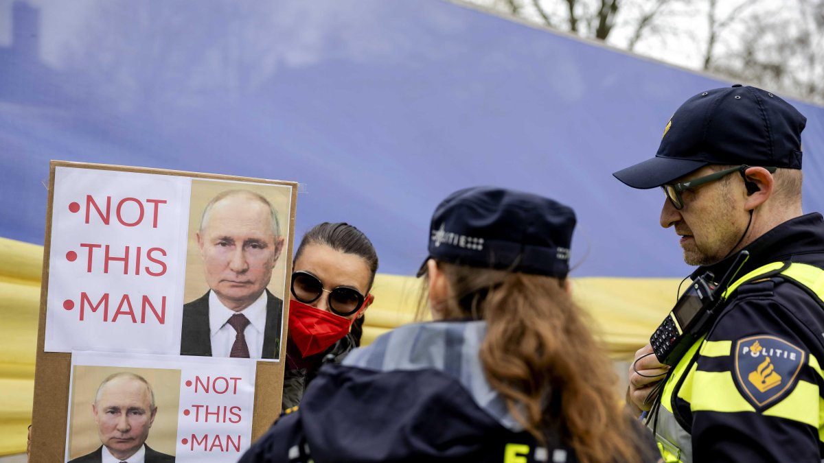 Una persona sostiene un cartel de protesta mientras los rusos esperan en fila para votar en la embajada rusa en La Haya, Países Bajos