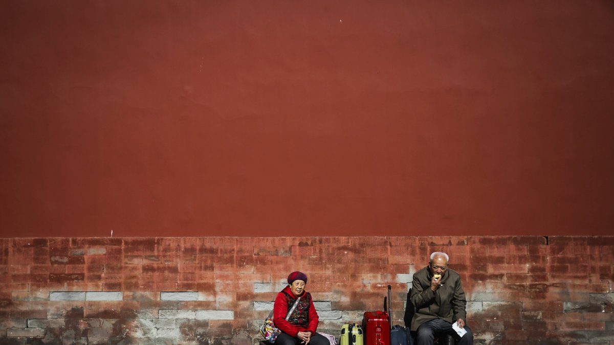 Una pareja de ancianos espera junto a su equipaje durante una visita a la Ciudad Prohibida en Pekín