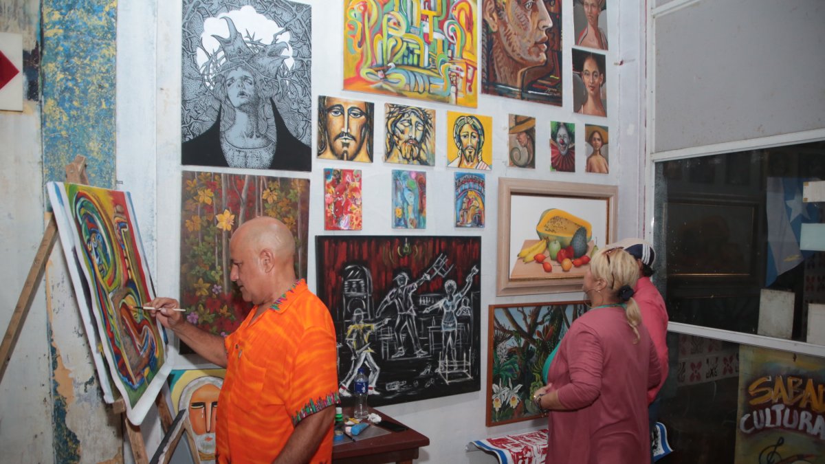 Arte. Jorge Ganín pinta un cuadro en el bar como parte de una muestra de su arte en vivo, mientras visitantes del sitio observan las obras.