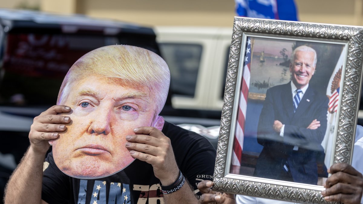 Washington. Dos personas aparecen con un retrato de Biden y una máscara de Trump, en media campaña.