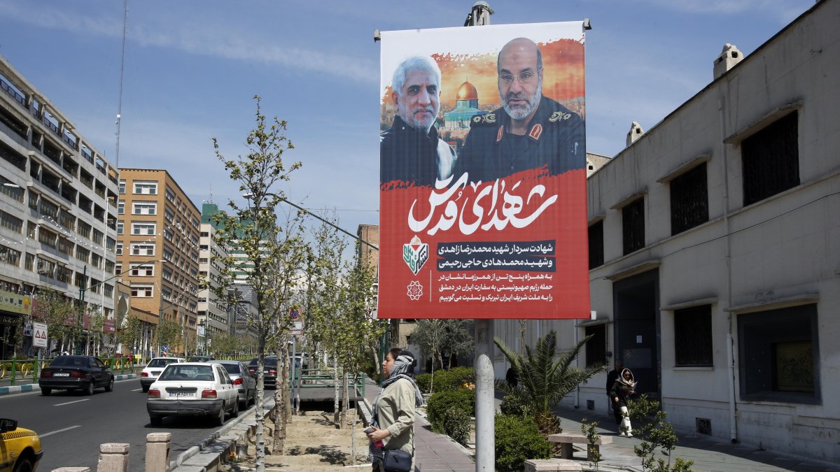 Una mujer pasa junto a un cartel que muestra fotografías del general de brigada iraní Mohammad Reza Zahedi (R), comandante de los Quds del Cuerpo de la Guardia Revolucionaria Islámica (CGRI)