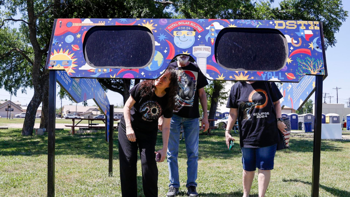 Una familia mira a través de un par de gafas gigantes especiales para el eclipse solar en el Veterans Memorial Park en Dripping Springs, Texas