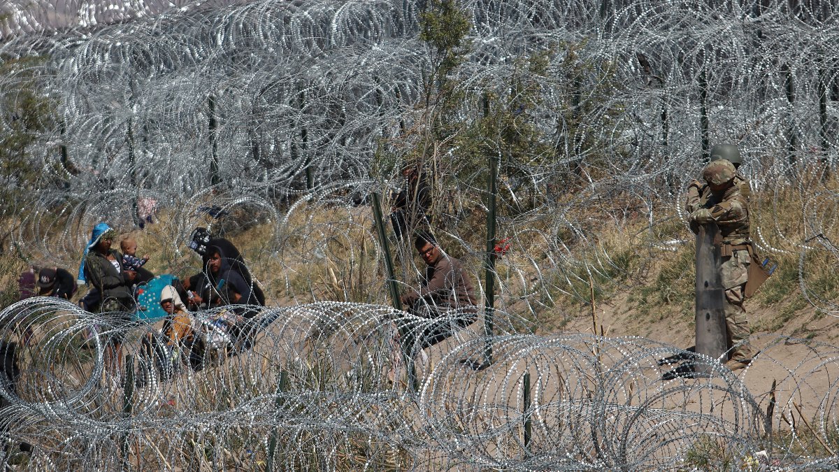 Migrantes esperan entre los alambres de púa mientras un agente estadounidense vigila, el 5 de abril de 2024, en Cudad Juárez,