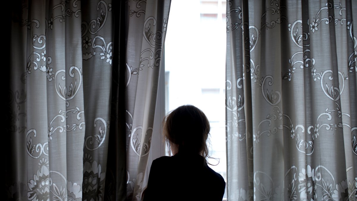 Una mujer observando a través de la ventana de su vivienda mientras permanece confinada por la crisis del coronavirus