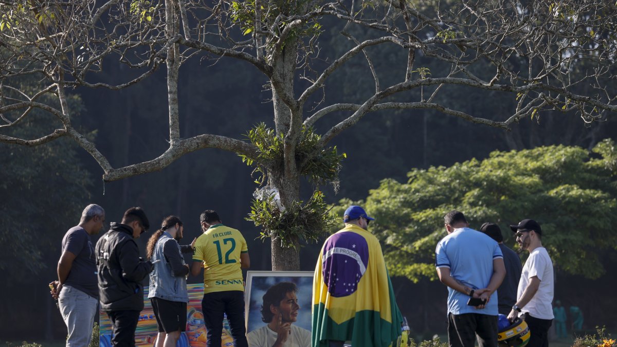 Seguidores del automovilista brasileño Ayrton Senna muestran respeto frente a la tumba del piloto