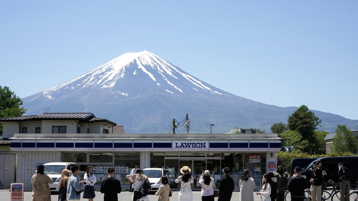 Turistas hacen fotografías de la tienda de la cadena Lawson con el Monte Fuji al fondo, en Fujikawaguchiko, al norte del Monte Fuji, Japón, el 10 de mayo de 2024.
