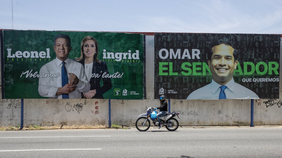 Una persona en una motocicleta pasa junto a un cartel de campaña electoral este domingo, en Santo Domingo (República Dominicana).