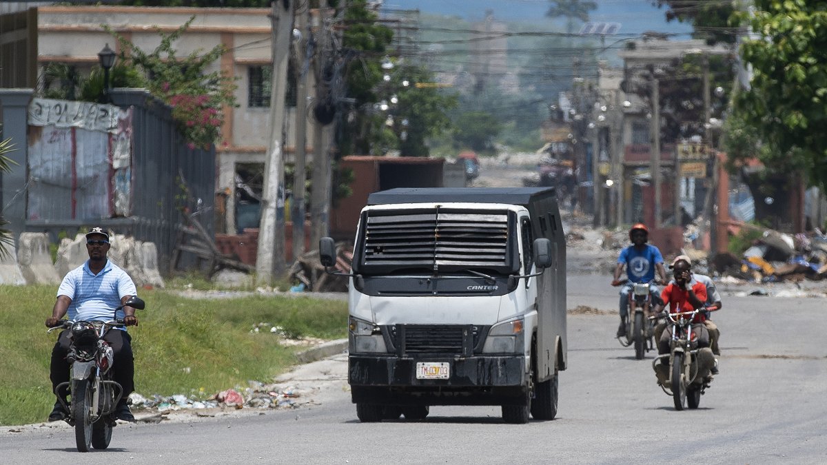 Motociclistas transitan junto a un carro blindado de la Policía Nacional Haitian.