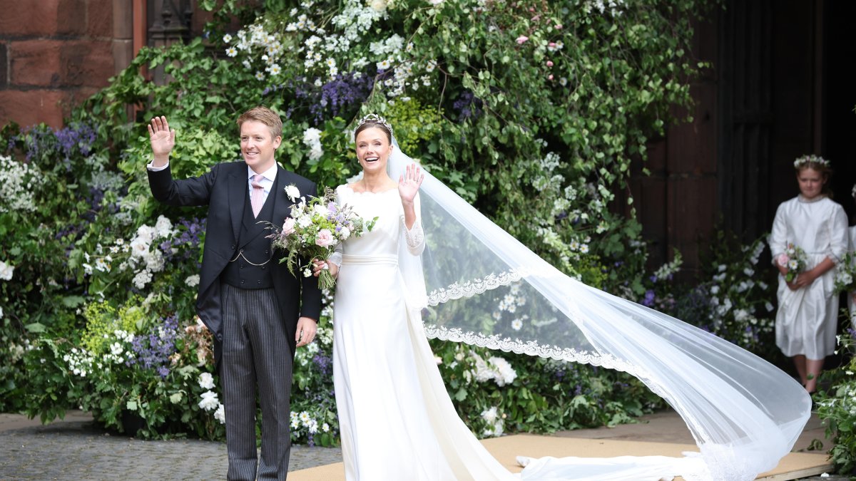 Olivia eligió un traje clásico: recto, escote discreto y manga larga, repleto de encajes. La hombreras bien marcadas y la larga cola complementaron el bellísimo traje de novia. Recogió su melena con un moño alto, y rompió el look con zapatos azules. Debajo del velo, se veía la tiara Myrtle Wreat, pieza de la colección Westminster, elaborada en 1906 por el joyero ruso Fabergé.