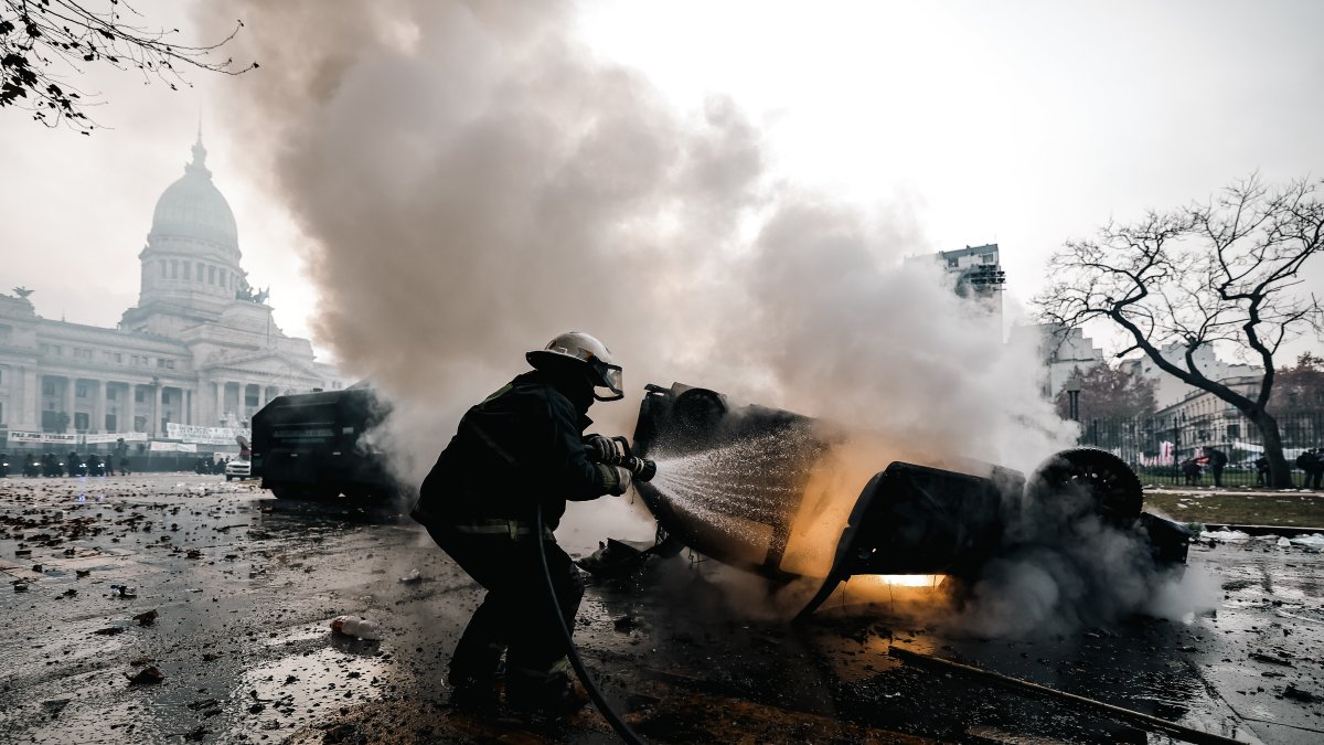 Un bombero apaga un auto en llamas durante enfrentamientos entre la policía y personas que protestan a las afueras del senado durante un debate este miércoles, en Buenos Aires (Argentina). 