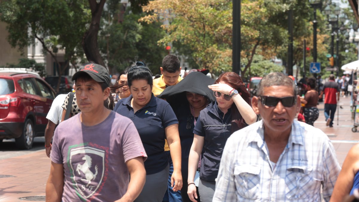 Soleado. Varias personas acelerando el paso en una calle principal de Guayaquil, para evitar el fuerte sol.